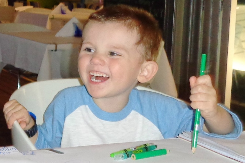 William Tyrrell sits at a table, smiling and holding a pen.