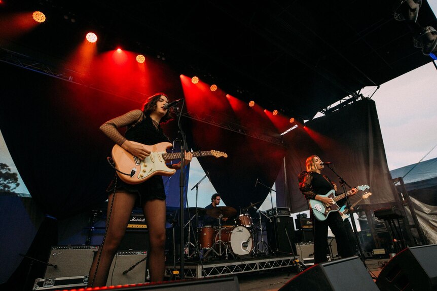 Two girls playing guitar on a festival stage singing.