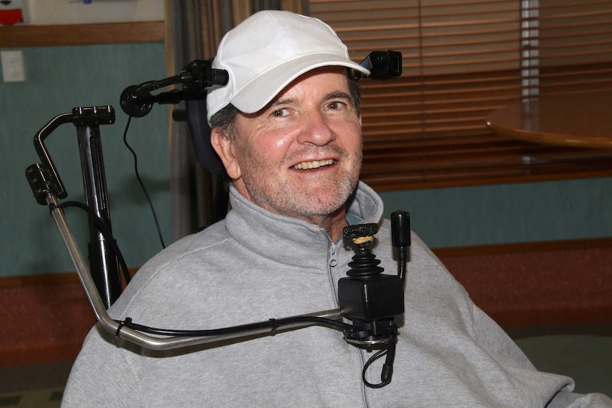 Mick McKay wearing a white cap and grey jumper sitting in a wheelchair.