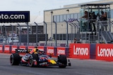 A blue F1 car drives past the finish line, with a chequered flag being waved.