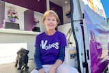 Jo Westh wears a purple shirt with 'Voices' written on it, sitting in her van with her dog.