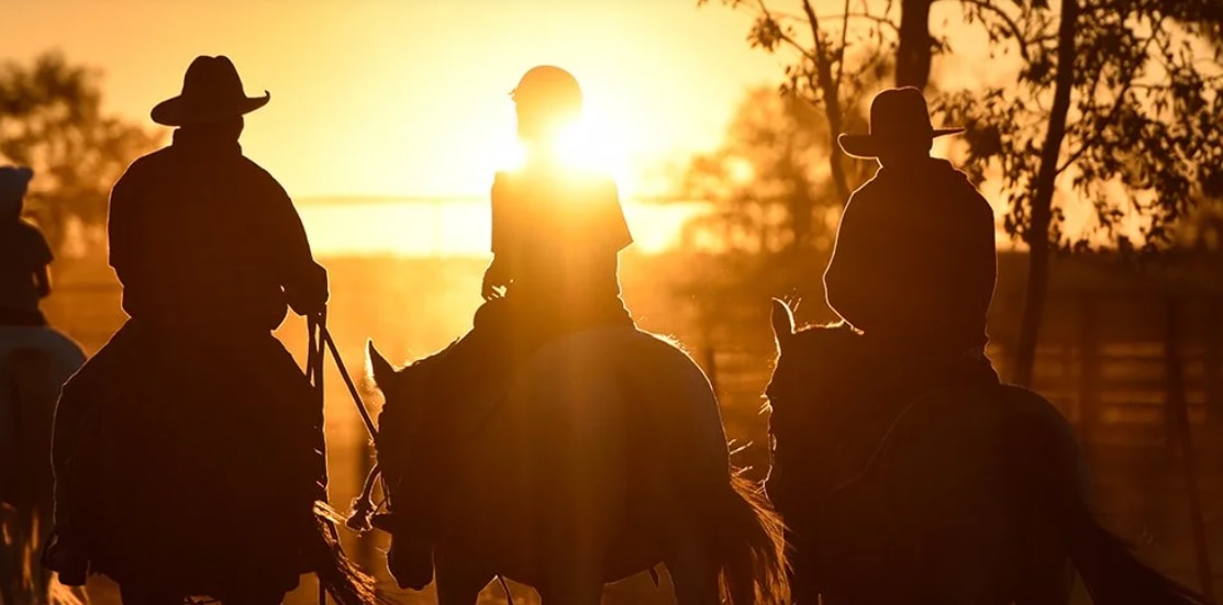 three people on horses at sunset