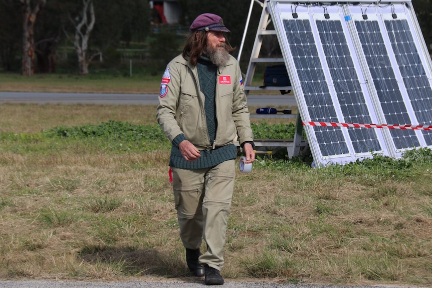 Fedor Konyukhov walks on a grass field in Northam wearing a green jacket and pants and a purple hat.