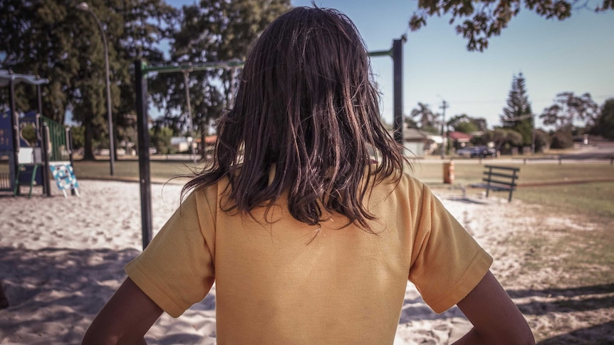 A Indigenous child faces away from the camera in a playground.