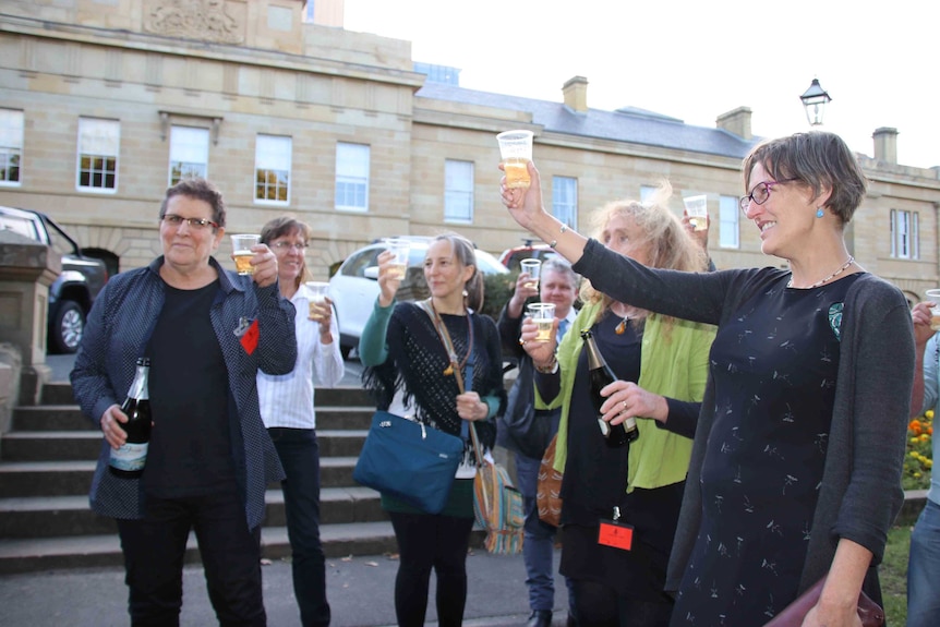 Des gens qui lèvent des verres devant le Parlement de Tasmanie.