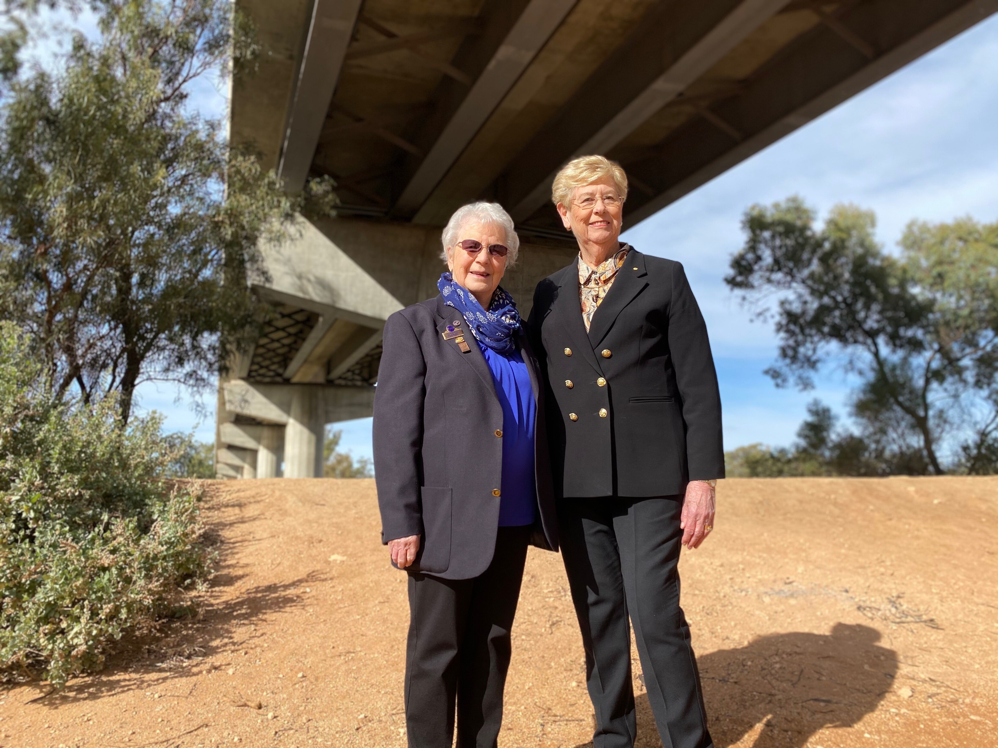 Two women stand together underneath a large bridge