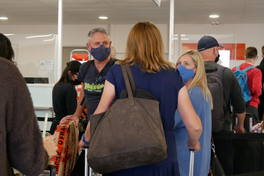 Passengers wearing masks, carrying bags line up in the airport.