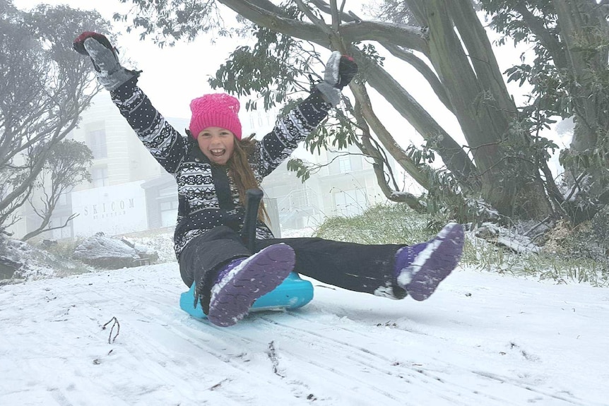 A 10-year-old girl rides a toboggan in light snow at Mount Hotham.