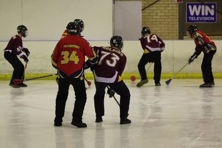 um grupo de jogadores em uma pista de gelo usando vassouras para acertar uma bola laranja