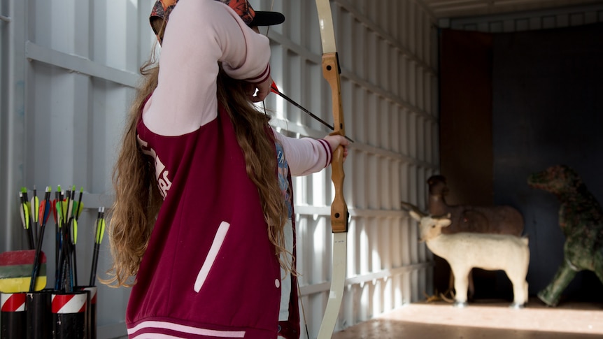 A female aiming a bow and arrow at a fake dear.