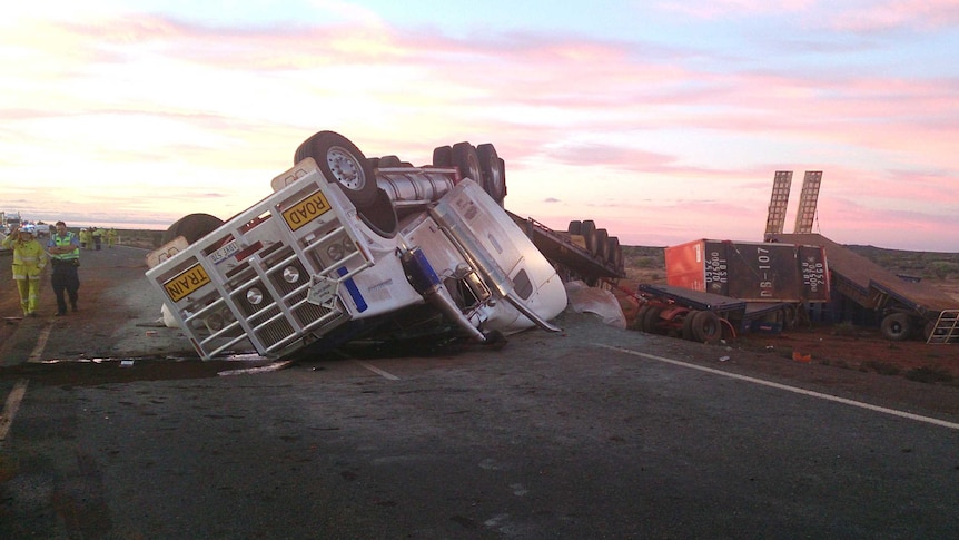 A truck driver walks away from the wreckage of his overturned road train.