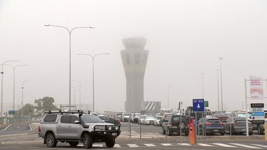 An airport tower in fog and a car park