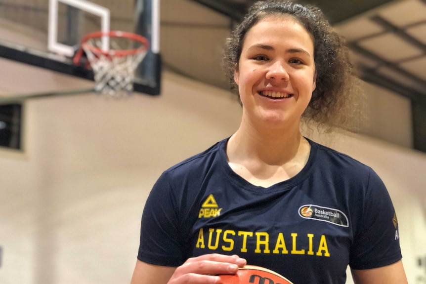 A young woman holds a basketball and smiles