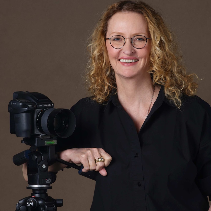 The photographer Anne Geddes posing next to a camera on a tripod