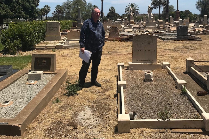 A man walks in a graveyard, papers in hand.