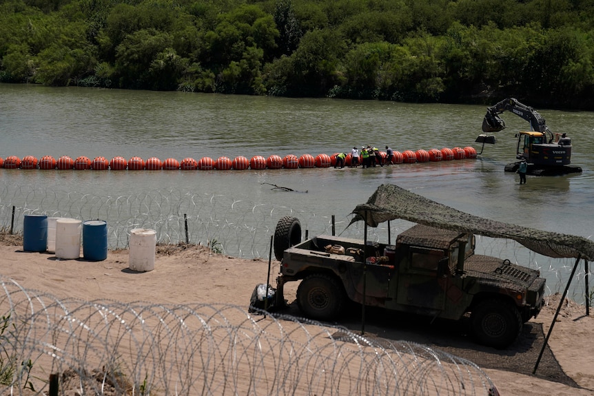 Large orange buoys float in the water and razor wire blocks part of the river off from access.. 