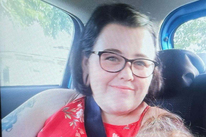 A woman wearing glasses and a red shirt sitting in a car. 