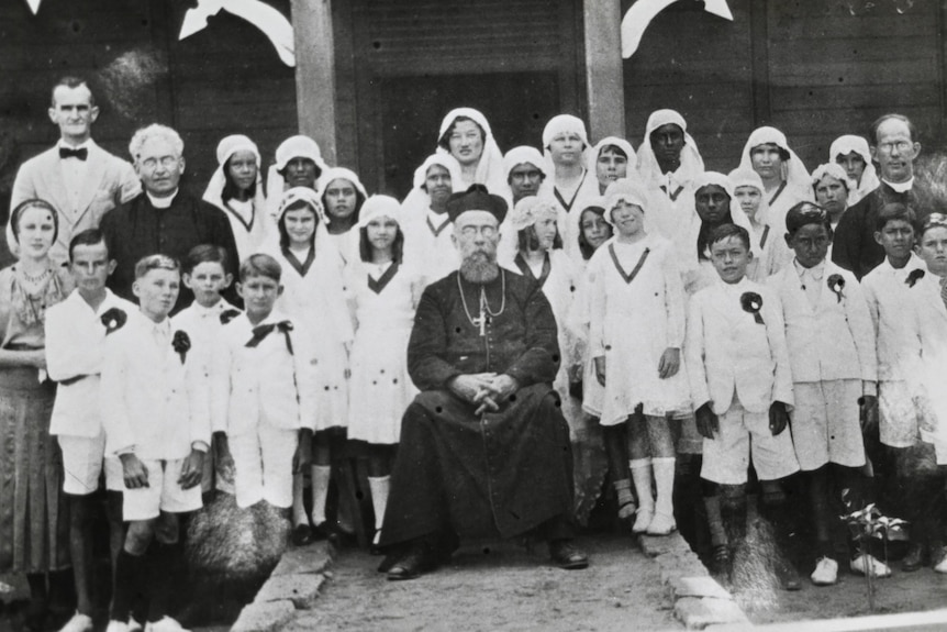 Black and white image of a church bishop surrounded by children wearing white clothing 