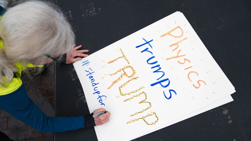 Women writes on her sign for the Stand up for Science rally in Boston