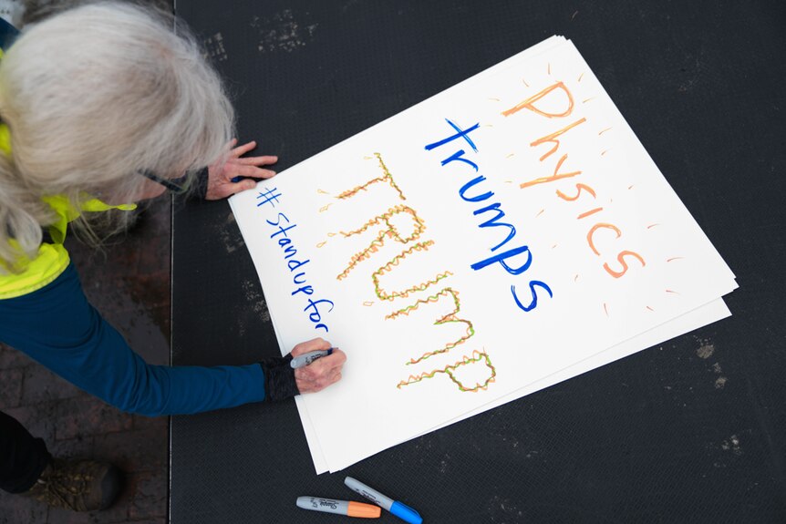 Women writes on her sign for the Stand up for Science rally in Boston