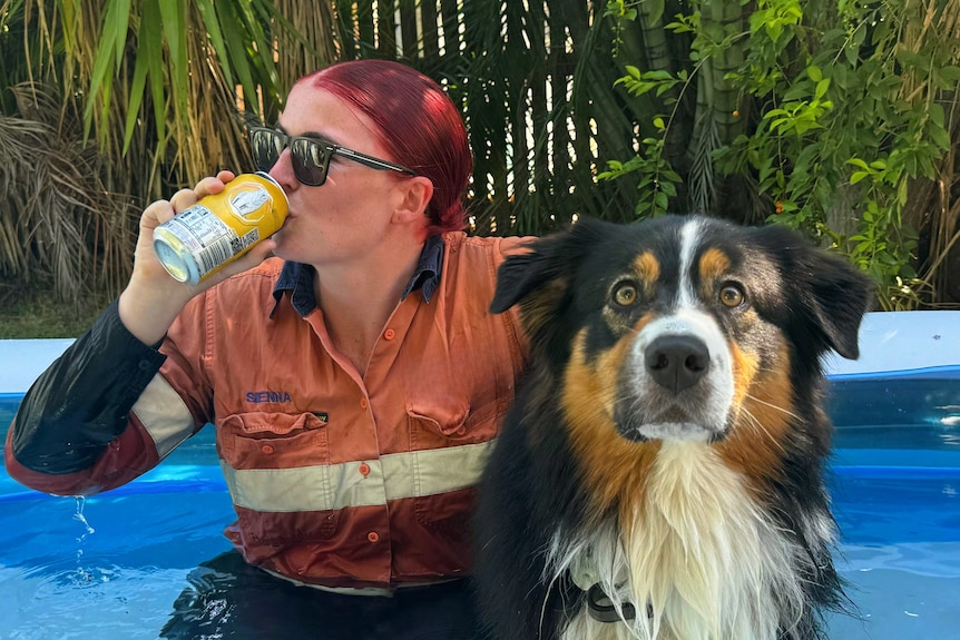 Woman drinks a can of drink in blow up pool with a dog