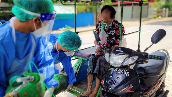 Two doctors in PPE assist with a oxygen tank for a man next to his motorcycle.