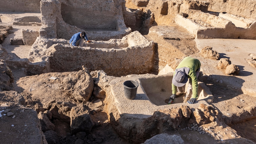 Two men wearing gloves conduct excavation work among the ruins of an ancient winery