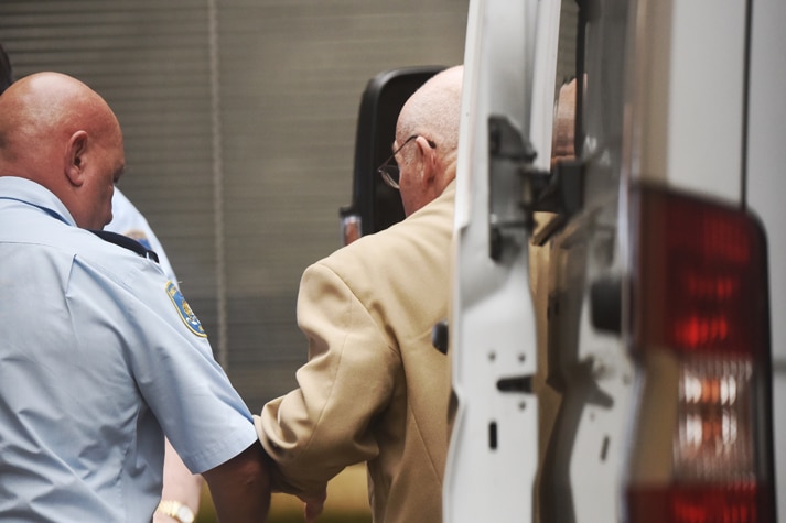 Back view of Roger Rogerson being led from a prison van to an exterior door of the court.