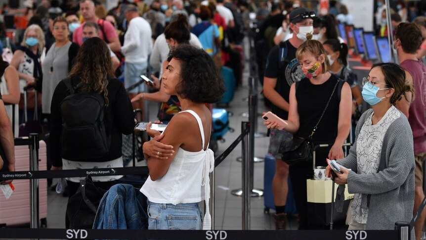 People try to social distance as they line up in crowds at Sydney Airport.