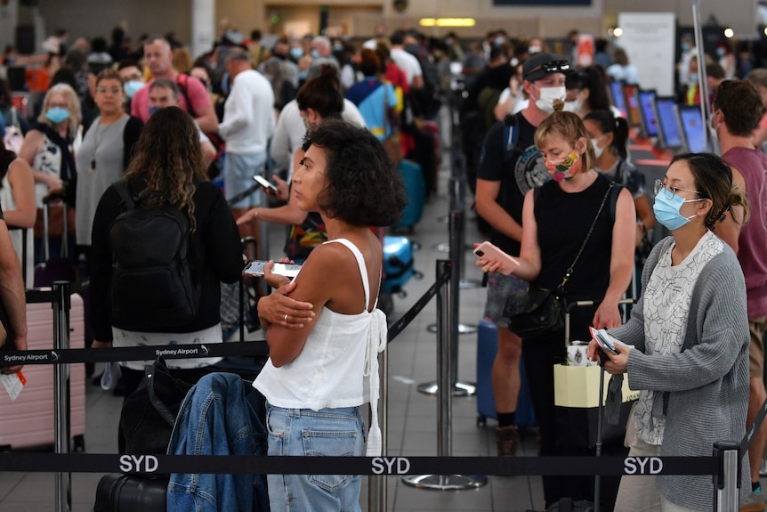 People try to social distance as they line up in crowds at Sydney Airport.