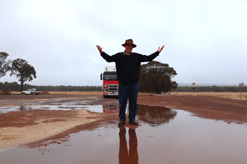 A farmer stands in a huge puddle with his hands in the air.