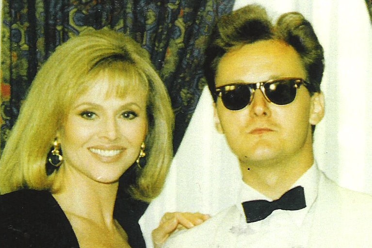 A blonde woman in a black suit standing next to a man in sunglasses.