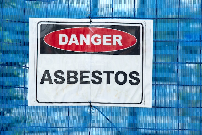 A blue netting fence with a sign saying danger asbestos