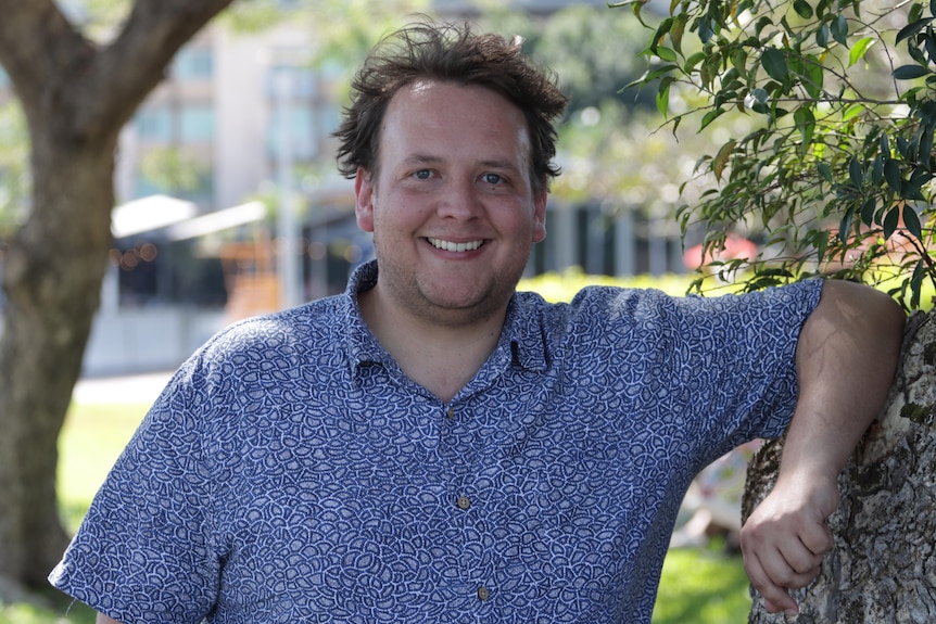 Man puts left arm on tree and looks forward to smile