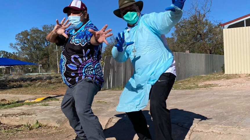Two men pose for a photo in Wilcannia, one wearing personal protective equipment 