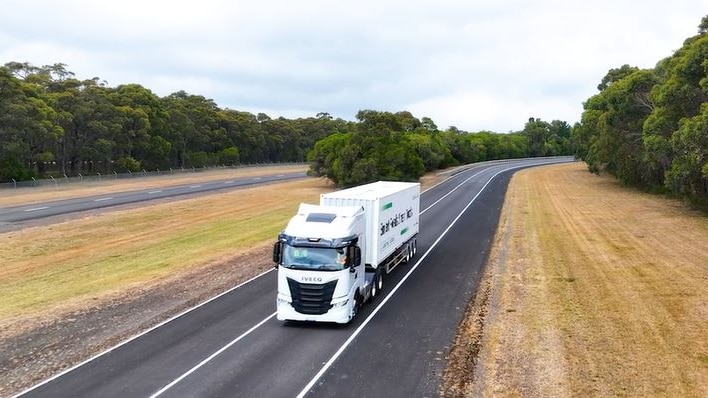 White truck driving down an empty highway surrounded by trees