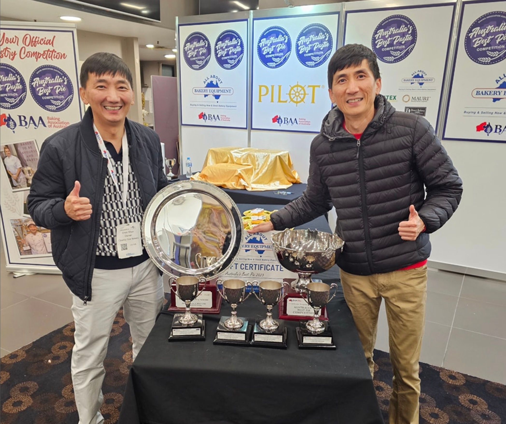 Two men stand at a table with a number of trophies.