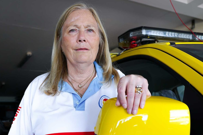 A woman stands with her hand resting on the side mirror of a Surf Living Saving vehicle.