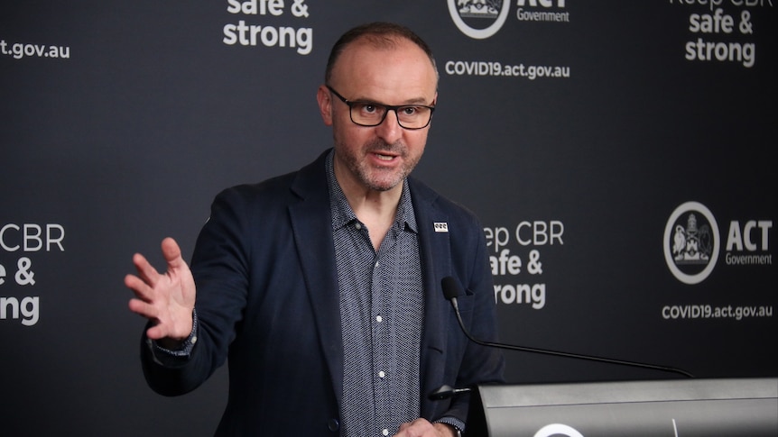 A man in glasses and a suit speaks at a podium.