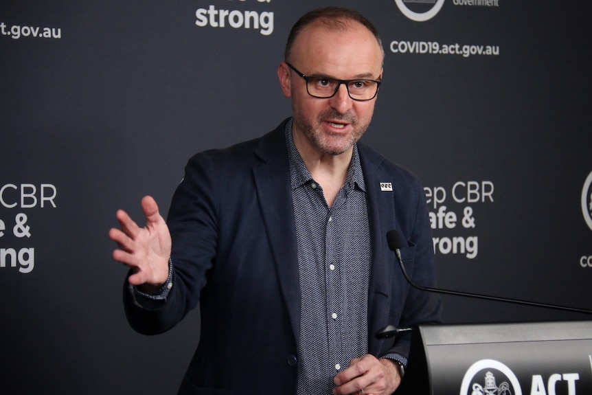 A man in glasses and a suit speaks at a podium.