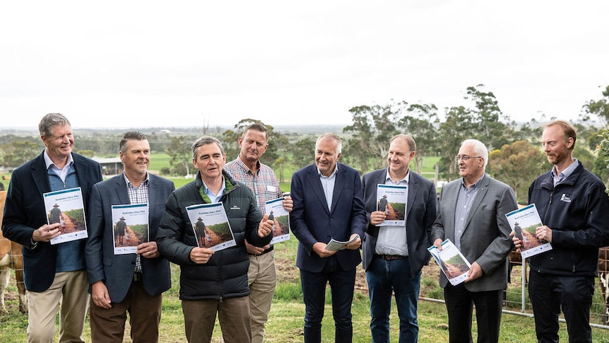 John Brumby and a group of men in suits holding copies of the draft document. Pictured with a dairy farm in background.