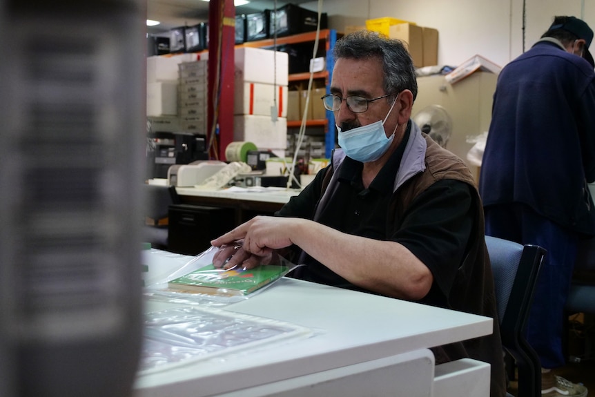 A man pushes a small green book into a plastic sleeve