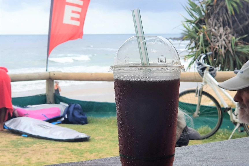a biodegradable plastic cup and straw in the foreground and ocean in the background