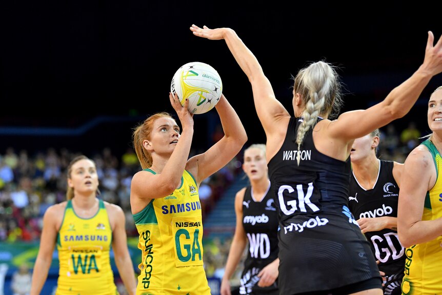 A woman holds a netball in her hands as another woman stands with her hand outstretched in front of her.