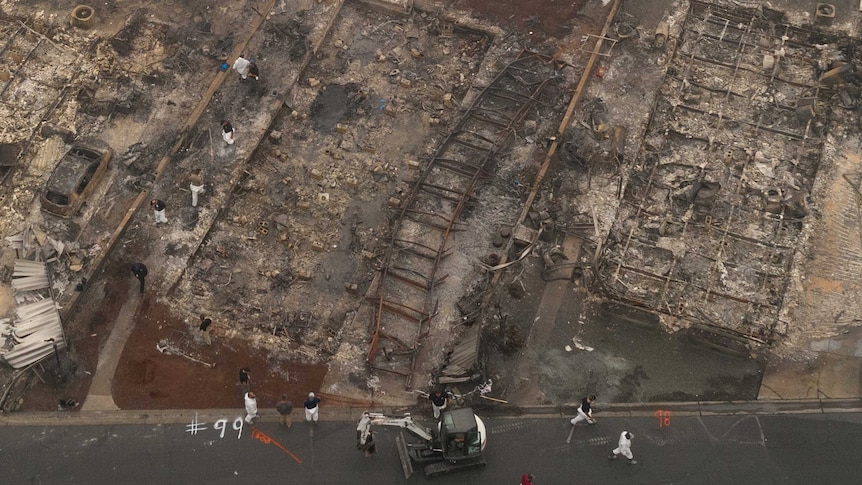 An aerial shot shows rescue workers in protective gear searching through the remains of burned out buildings.