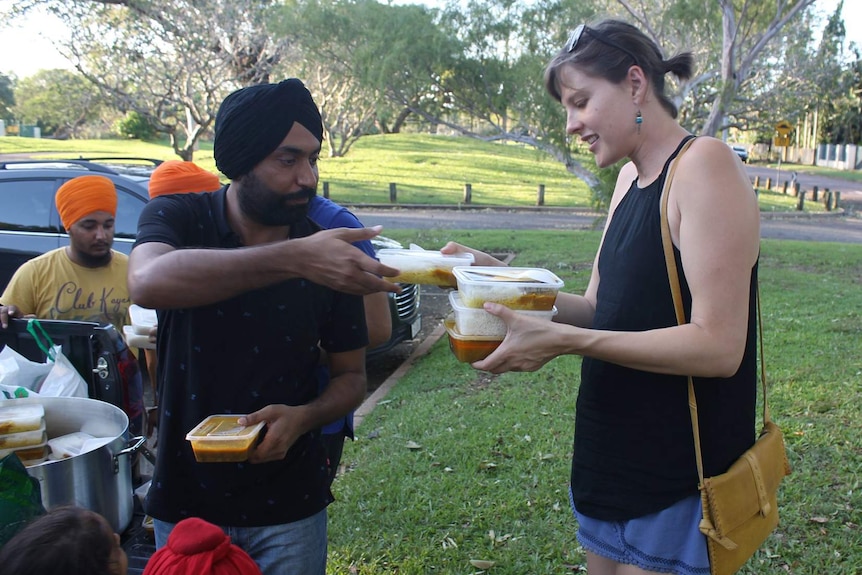 A man hands food containers to a woman in a park.