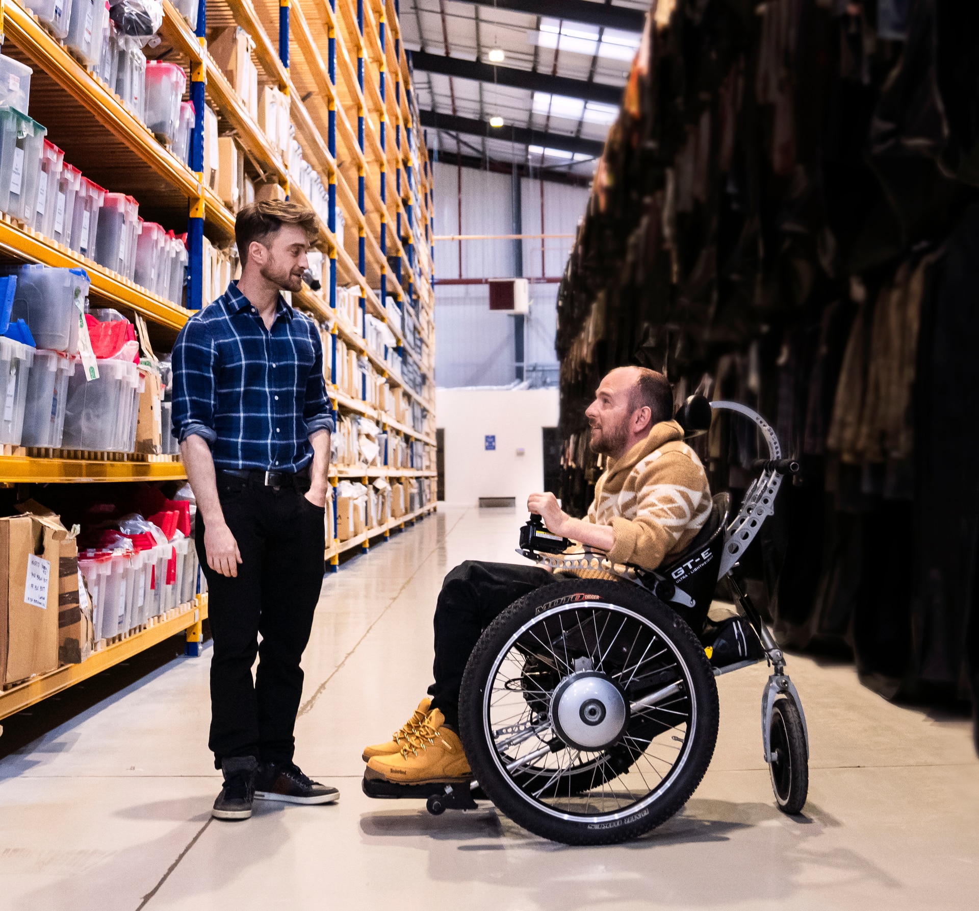 David, in a wheelchair, speaks to Daniel in a warehouse as Harry Potter costumes and props surround them.