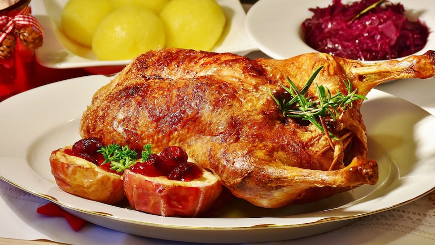 A roast duck sitting on a white china dish, with side dishes in the background.