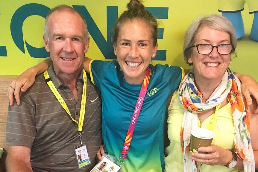 Jess sits in between her parents, wearing her Commonwealth Games uniform and lanyard.