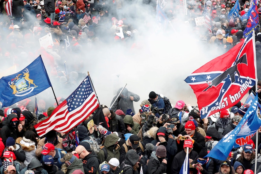 A huge crush of people wielding American flags and confederate flags in a haze of smoke 